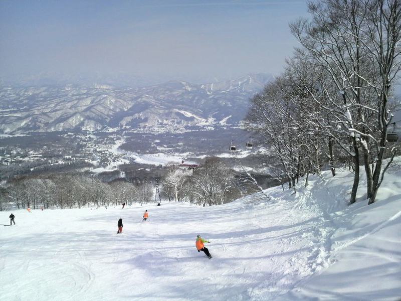 Skiers on a groomed run at Akakura, Myoko, looking out over snowy mountains